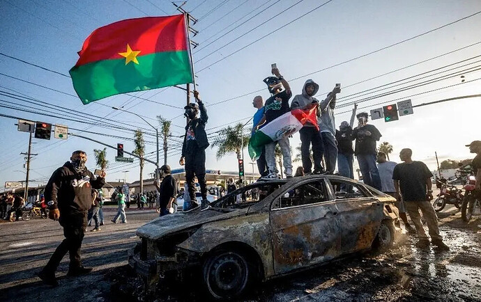 Protesters standing on top of a burned vehicle, reportedly used by ICE
